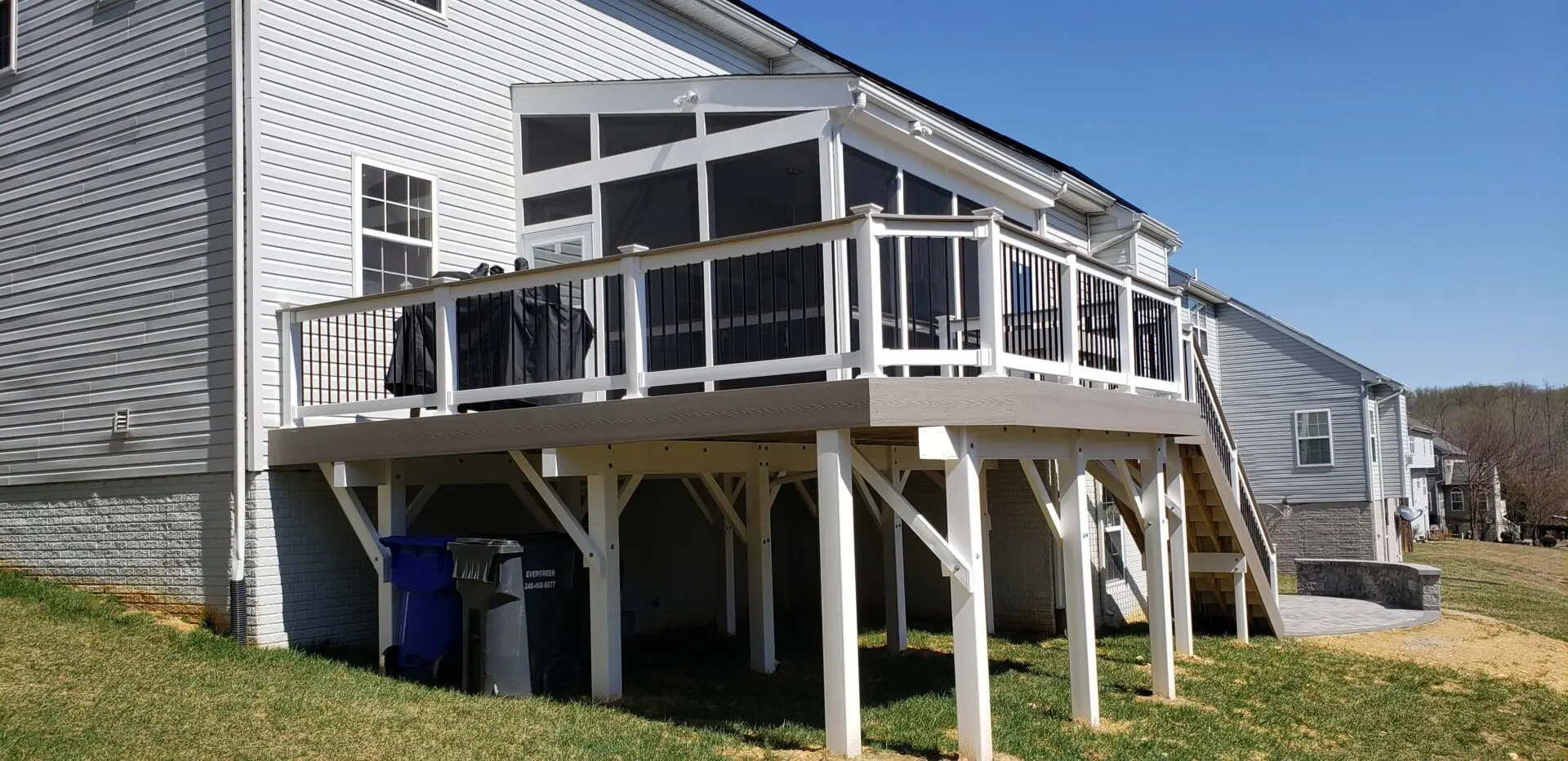 Raised screened porch attached to a white house with wooden railings and support beams.
