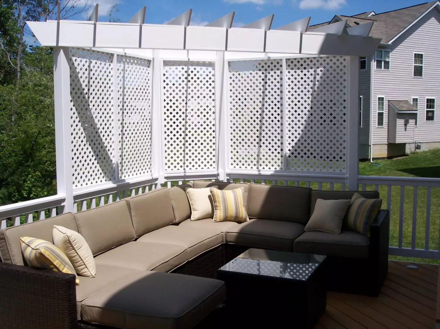 A deck with a brown couch and white pergola